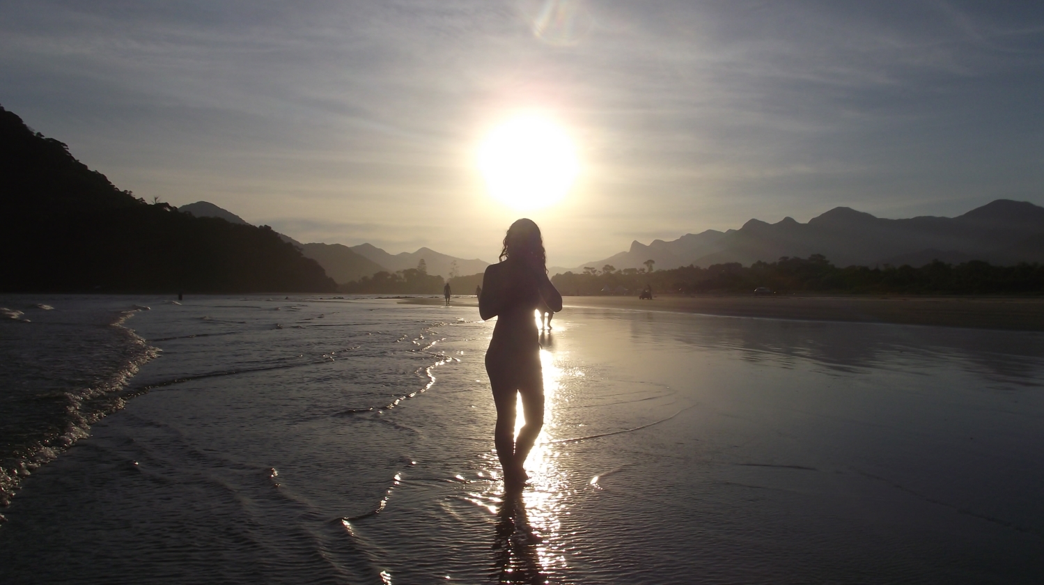 mulher sob a luz do sol da tarde na praia do guaraú e com morros e céu ao fundo