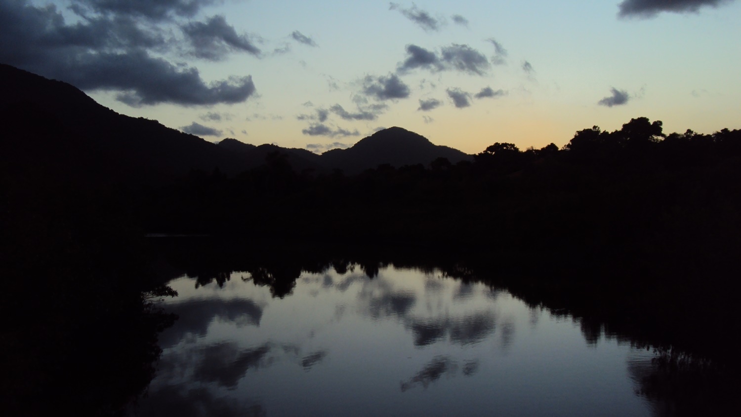 Lago refletindo o céu sombrio e morros escurecidos pelo anoitecer.